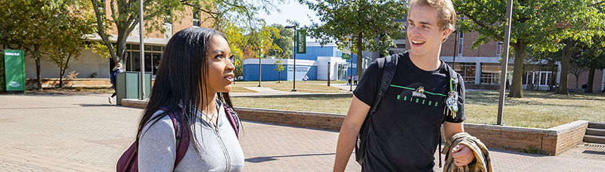 photo of two students walking and talking outside on campus