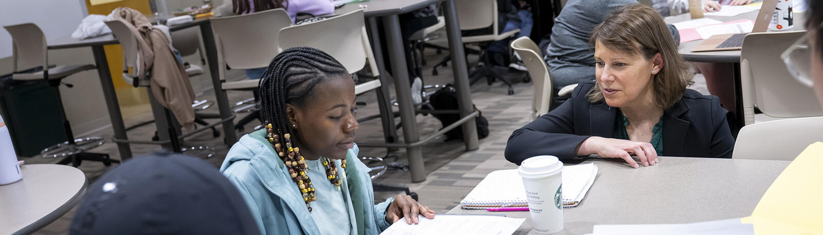 photo of a professor talking to students sitting at a table in a classroom
