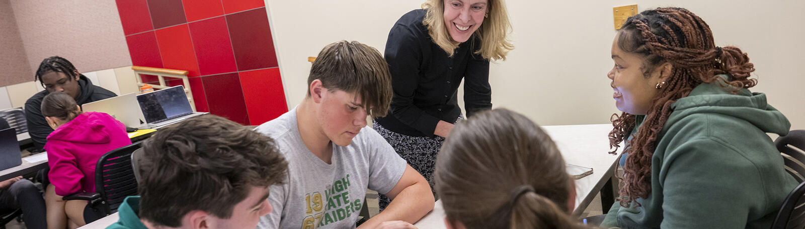 students and a professor gathered at a table in a classroom