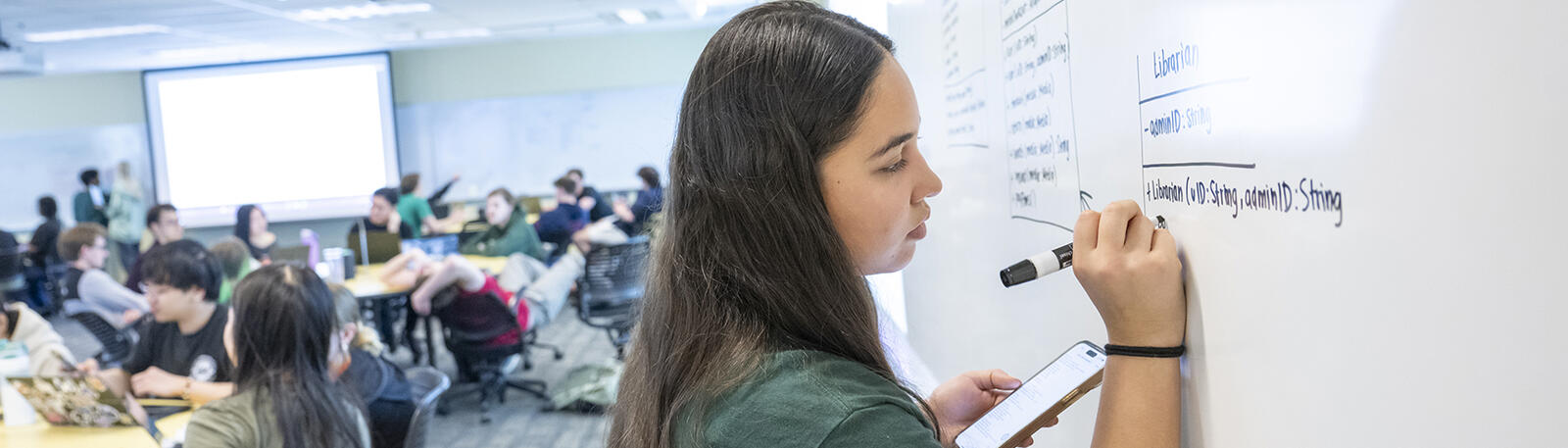 a teacher education student writing on a whiteboard in a classroom