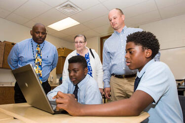 photo of students and teachers looking at a laptop